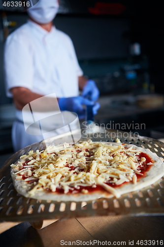 Image of chef  with protective coronavirus face mask preparing pizza