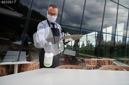 Image of Waiter cleaning the table with Disinfectant Spray in a restauran