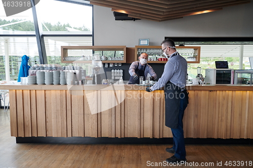 Image of waiter in a medical protective mask serves  the coffee in restau