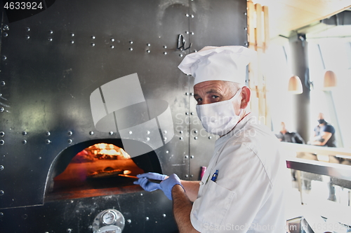 Image of chef  with protective coronavirus face mask preparing pizza