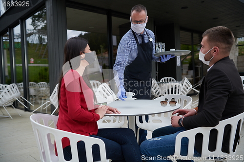 Image of Waiter with protective medical mask and gloves serving guest