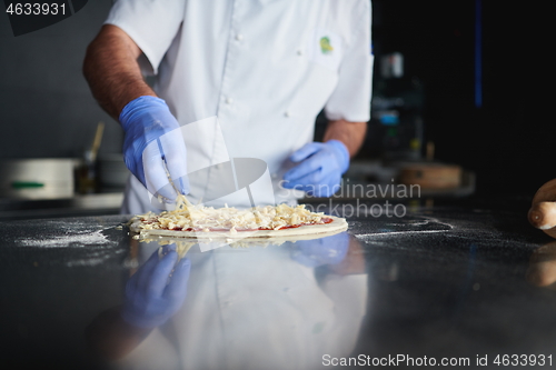 Image of chef  with protective coronavirus face mask preparing pizza