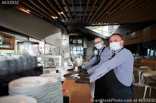 Image of waiter in a medical protective mask serves  the coffee in restau