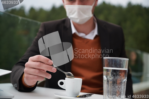 Image of man in restaurant drinking coffee wearing face mask