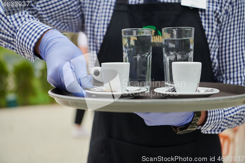 Image of waiter in a medical protective mask serves  the coffee in restau