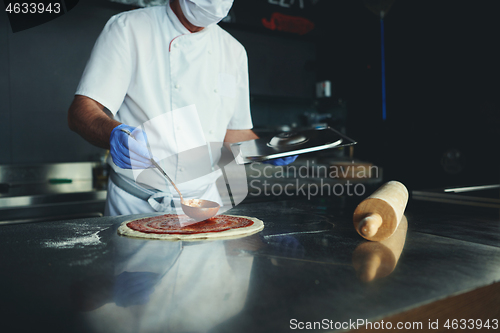 Image of chef  with protective coronavirus face mask preparing pizza