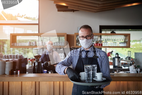 Image of waiter in a medical protective mask serves  the coffee in restau