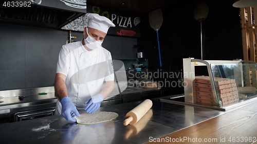 Image of chef  with protective coronavirus face mask preparing pizza