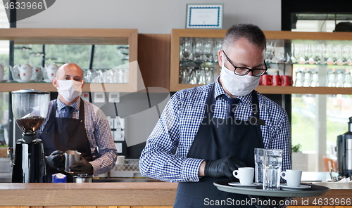 Image of waiter in a medical protective mask serves  the coffee in restau