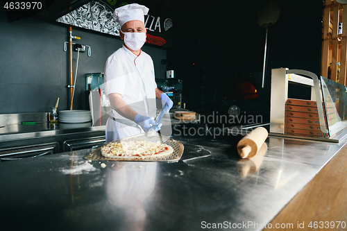 Image of chef  with protective coronavirus face mask preparing pizza