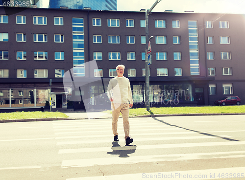 Image of senior man walking along city crosswalk