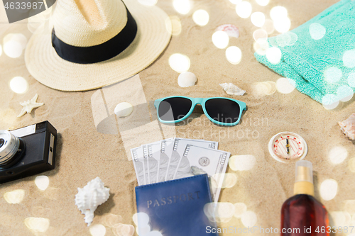 Image of money in passport, shades and hat on beach sand