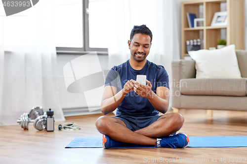 Image of indian man with smartphone on exercise mat at home