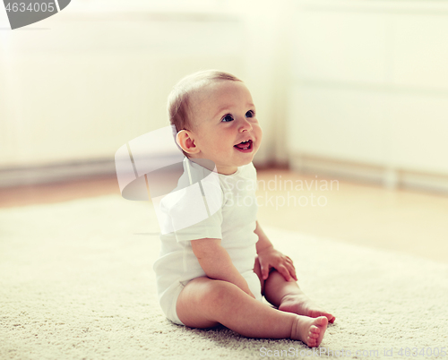 Image of happy baby boy or girl sitting on floor at home