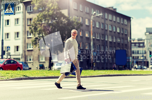 Image of senior man with shopping bags walking on crosswalk