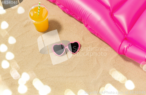 Image of sunglasses, juice and pool mattress on beach sand
