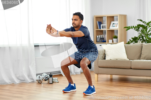 Image of indian man exercising and doing squats at home