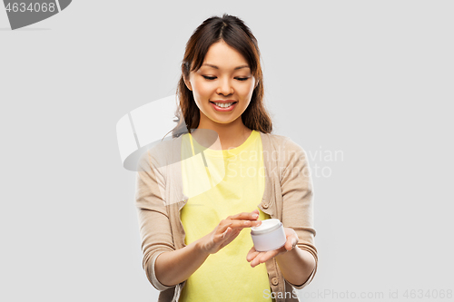 Image of happy young asian woman holding jar of moisturizer