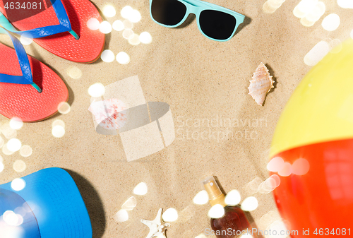 Image of cap, flip flops and shades and beach ball on sand