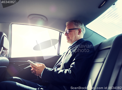 Image of senior businessman texting on smartphone in car