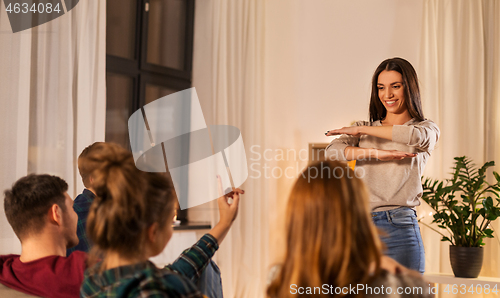 Image of happy friends playing charades at home in evening