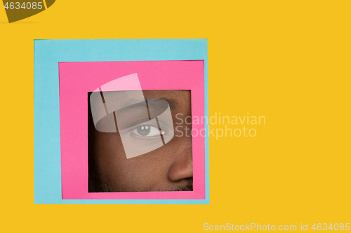 Image of Eye of african-american man peeking throught square in yellow background