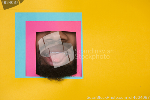 Image of Mouth of african-american man peeking throught square in yellow background