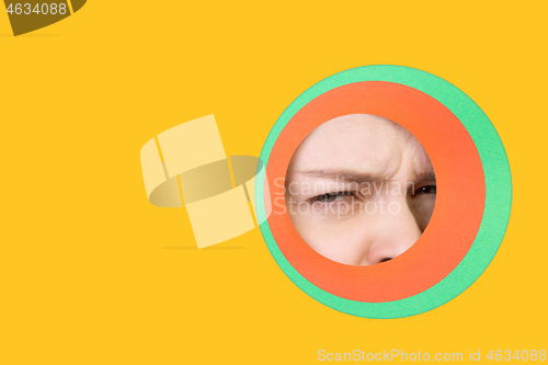 Image of Female eye peeking throught circle in yellow background