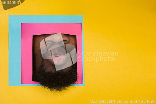 Image of Mouth of african-american man peeking throught square in yellow background