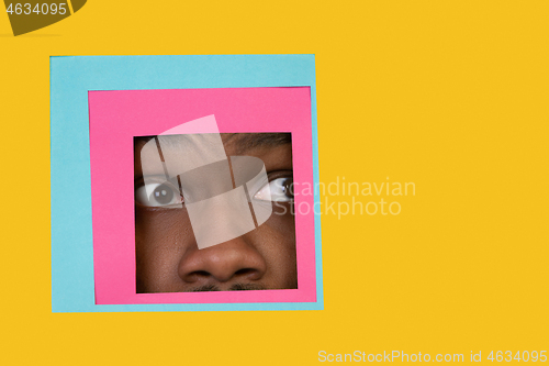 Image of Face of african-american man peeking throught square in yellow background