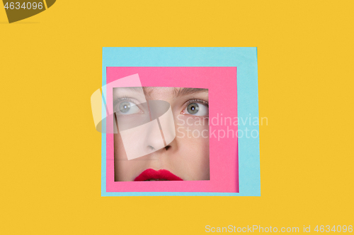 Image of Face of caucasian woman peeking throught square in yellow background