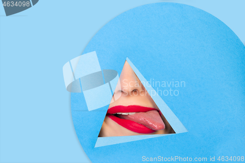 Image of Female red lips peeking throught triangle in blue background