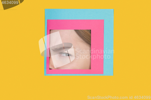 Image of Face of caucasian woman peeking throught square in yellow background