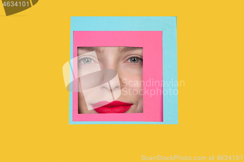 Image of Face of caucasian woman peeking throught square in yellow background