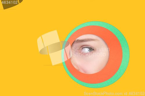 Image of Female eye peeking throught circle in yellow background