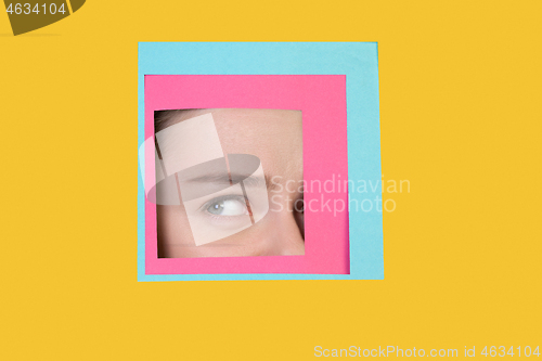 Image of Face of caucasian woman peeking throught square in yellow background