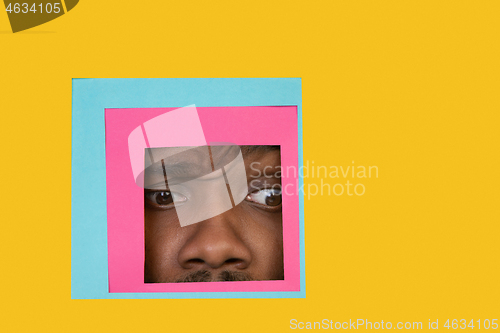 Image of Face of african-american man peeking throught square in yellow background