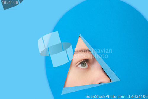 Image of Face of caucasian woman peeking throught triangle in blue background