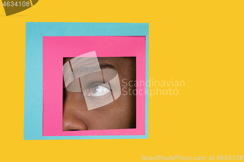 Image of Eye of african-american man peeking throught square in yellow background