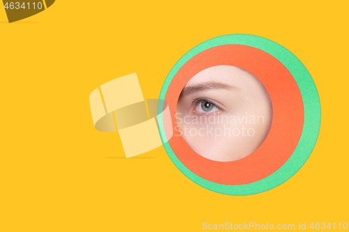 Image of Female eye peeking throught circle in yellow background