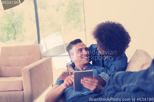 Image of multiethnic couple relaxing at  home with tablet computers