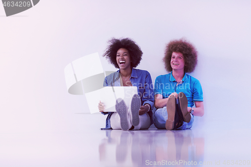 Image of multiethnic couple sitting on the floor with a laptop and tablet