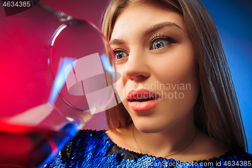 Image of The surprised young woman in party clothes posing with glass of wine.