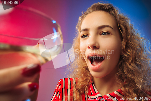 Image of The surprised young woman in party clothes posing with glass of wine.