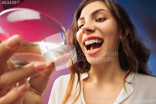Image of The surprised young woman in party clothes posing with glass of wine.