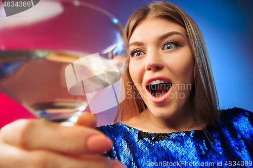 Image of The surprised young woman in party clothes posing with glass of wine.