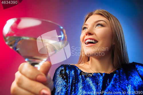Image of The surprised young woman in party clothes posing with glass of wine.