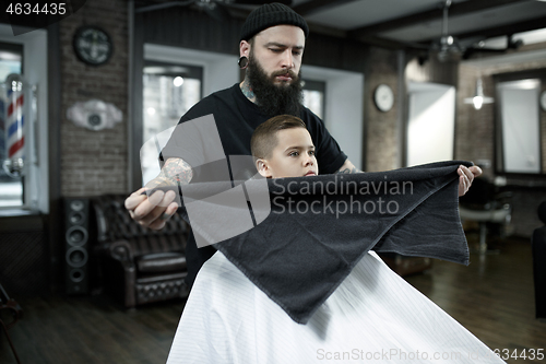 Image of Children hairdresser cutting little boy against a dark background.