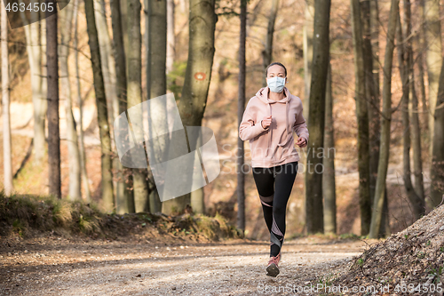 Image of Corona virus, or Covid-19, is spreading all over the world. Portrait of caucasian sporty woman wearing a medical protection face mask while running in nature.