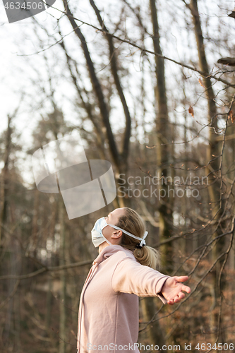 Image of Portrait of caucasian sporty woman wearing medical protection face mask while relaxing by taking a deep breath in forest. Corona virus, or Covid-19, is spreading all over the world